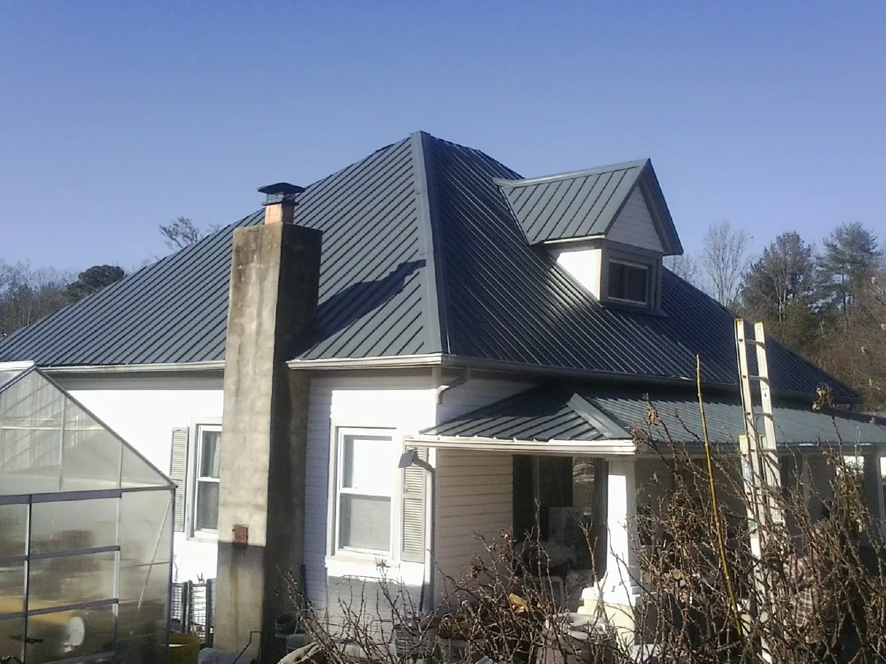 Dark blue standing seam metal roof on a white farmhouse with dormer — Slate & Tile Roof Repair by Roofing Brothers in Slate Hill