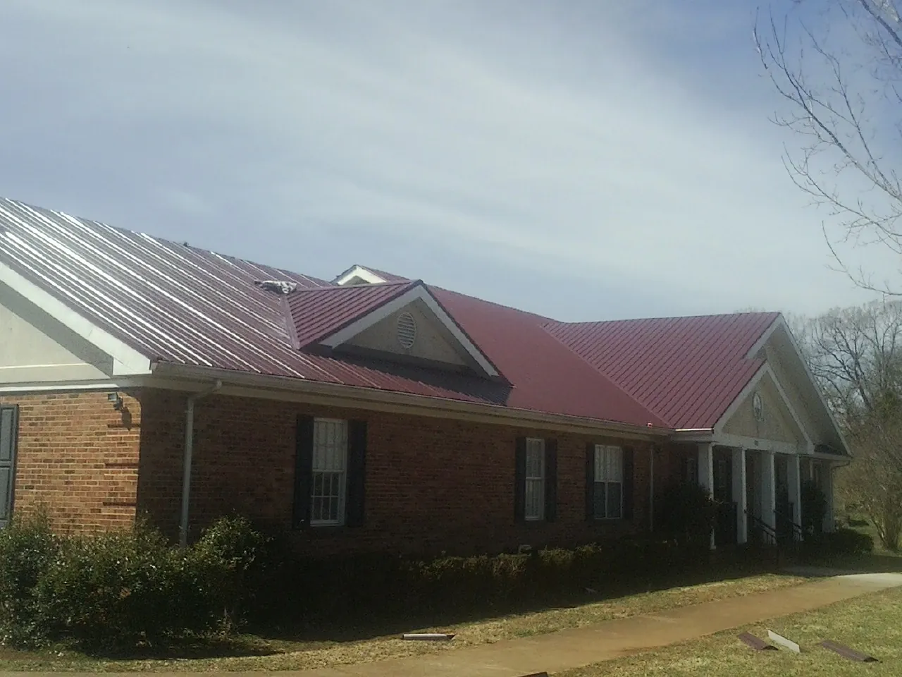 Red metal roof with gabled entries on a long brick building, from a Hail Damage Roof Repair job in Slate Hill