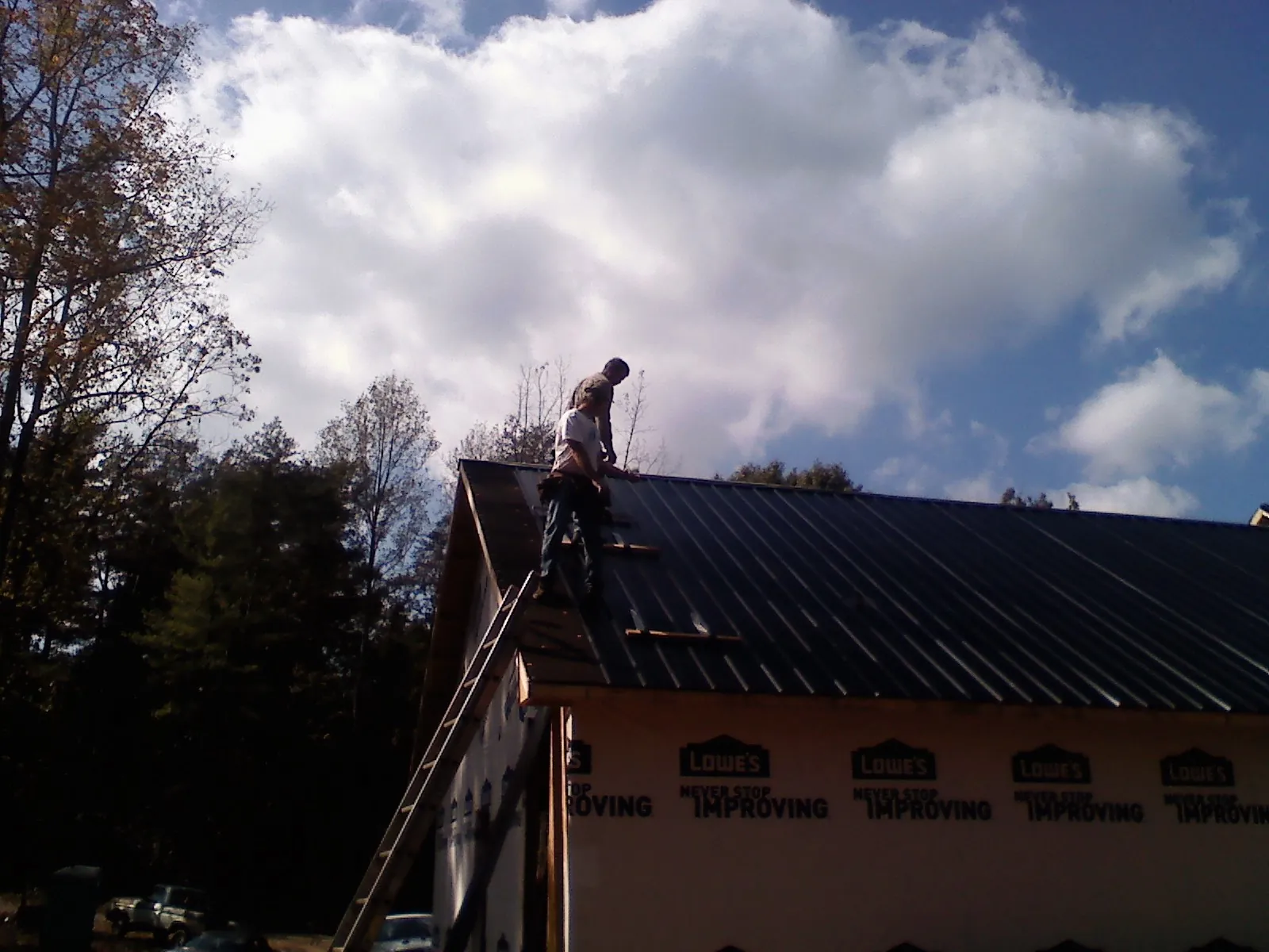 Roofer fastening dark metal panels high against a cloudy sky, from a Roof Inspection job in Slate Hill