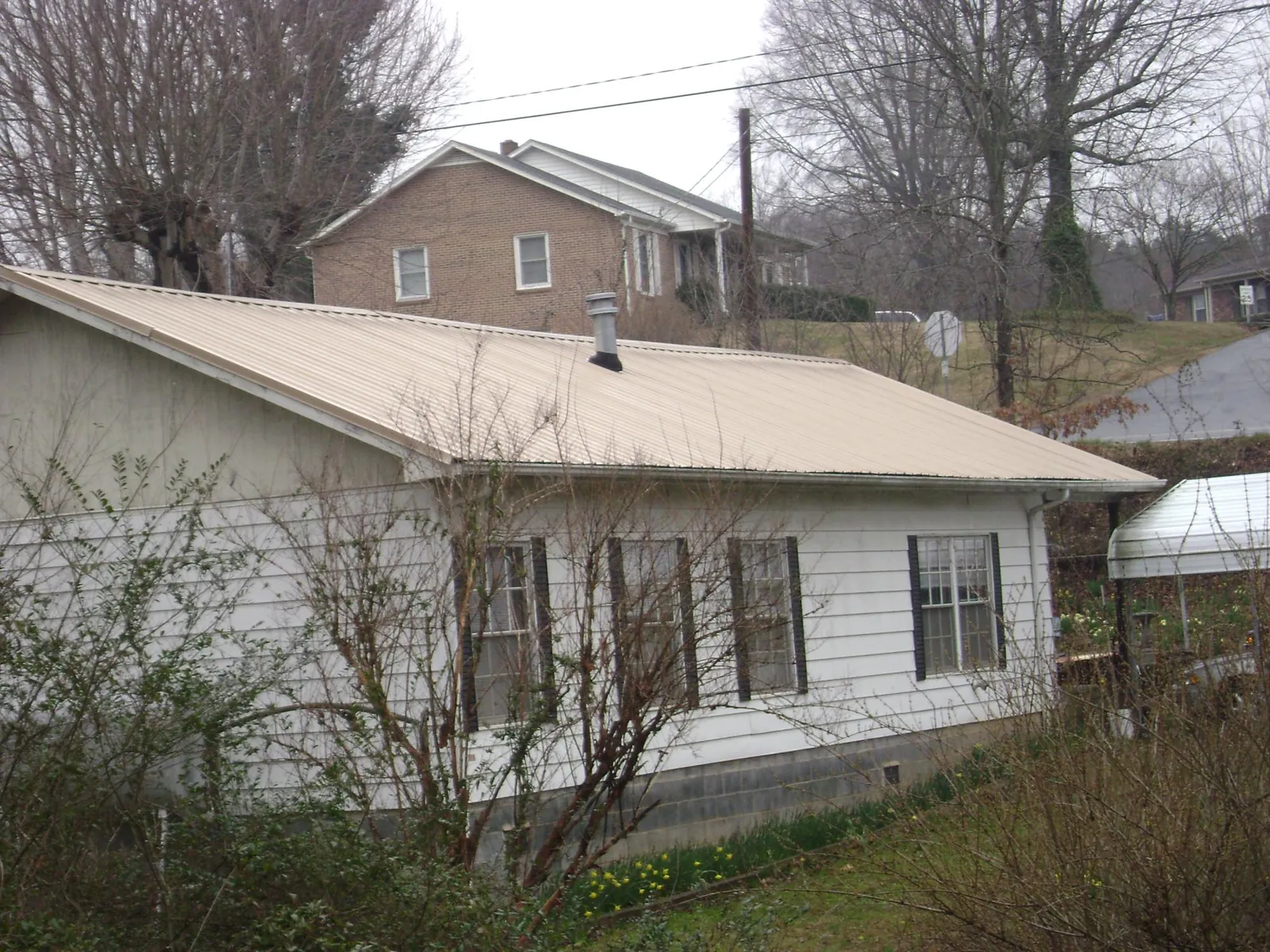Tan metal roof on a white sided house set into a hillside — Commercial Roofing by Roofing Brothers in Slate Hill